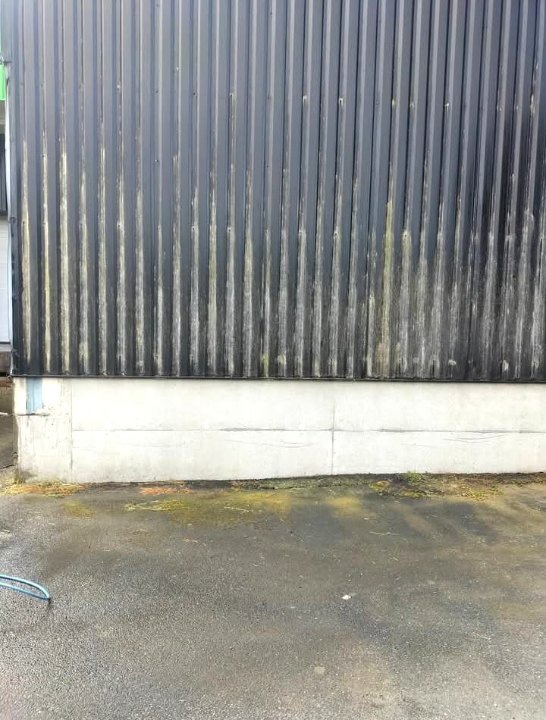 Bardage en bac acier noir strié de coulures blanches au-dessus d'un soubassement béton