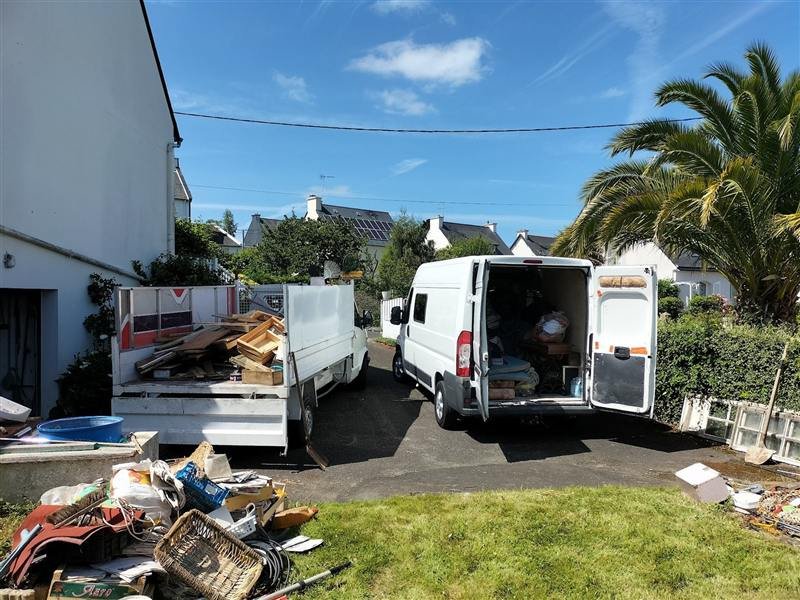 Camion-benne et fourgon chargés d'encombrants devant une maison