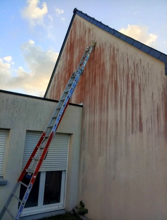 Pignon enduit strié de traces rouges, grande échelle posée contre le mur