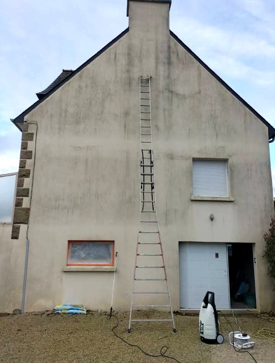 Haut pignon grisé et taché, échelle dressée jusqu'à la cheminée, nettoyeur au pied du mur
