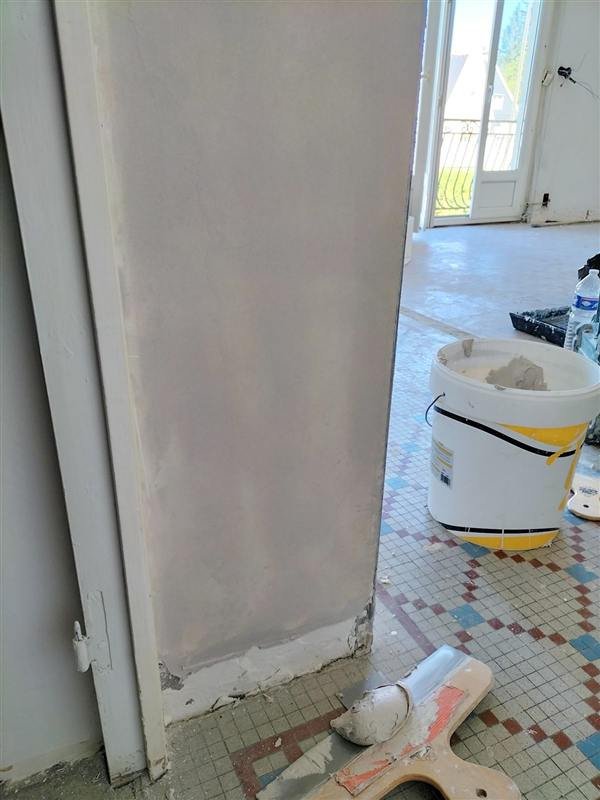Mur enduit et poncé avant peinture, seau d'enduit et outils au sol