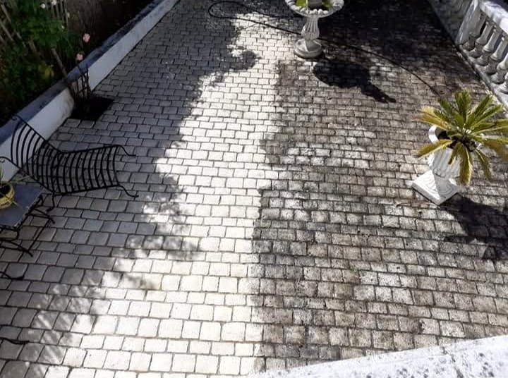 Terrasse en pavés en cours de nettoyage : la partie gauche, déjà traitée, est claire, la partie droite encore noircie